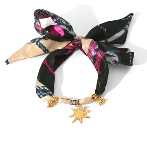Close-up of silk scarf bracelet with golden sun and heart charms on a white background