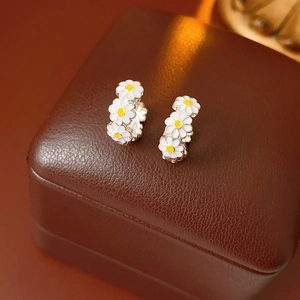 Macro detail of silver vintage daisy enamel earrings on brown leather jewelry box