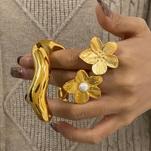 Golden flower ring with pearl and wavy open cuff bracelet on beige knitwear sweater