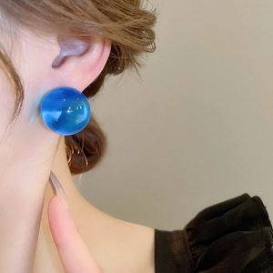Gros plan d'une boucle d'oreille sphérique en résine bleu Klein portée pour un look chic
