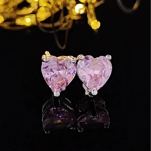 Detailed close-up of pink heart-shaped crystal stud earrings on black mirror surface