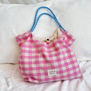 Detailed view of pink and beige plaid tote bag with blue rope handles on white bedding