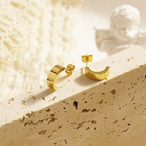 Minimalist 18K gold plated C-shaped stud earrings on a vintage beige travertine stone