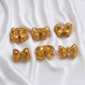 Golden stainless steel bow-knot jewelry charms on elegant white silk fabric background