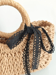 Handcrafted woven straw tote bag with black lace bow and round handle for beach vacations