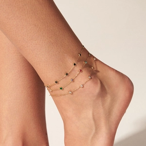 Detail of a multi-layer gold anklet with colorful round stones on a woman's ankle