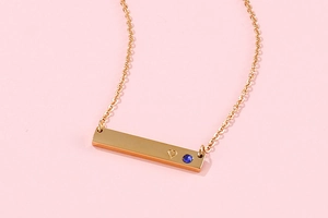 Close-up of gold bar pendant necklace with heart engraving and blue gemstone