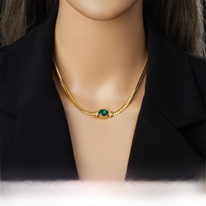 Detail of a gold snake chain necklace with an oval emerald green stone on a black blazer