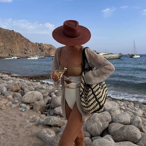 Chic women's beach set featuring a hollow swimsuit, wide-brim hat, and woven tote bag on a coast