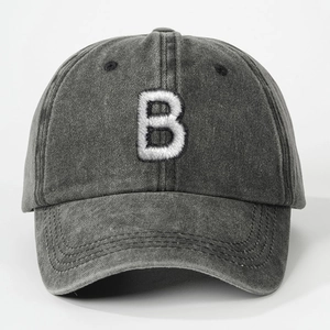 Detailed close-up of white embroidered letter B on washed charcoal grey baseball cap fabric