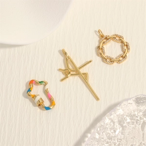 Three gold micro-pave zircon pendants including a cross and enamel clasp on beige texture