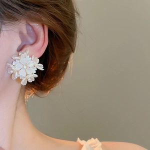 Close-up of elegant white floral stud earrings with pearl luster on a female model