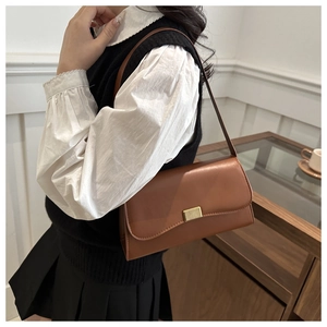 Brown faux leather shoulder bag with gold buckle shown on model in retro setting