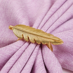 Elegant gold feather alloy napkin ring displayed on a light purple linen napkin cloth