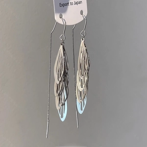 Détail de boucles d'oreilles longues argentées avec design de feuilles ciselées en métal