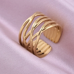 Macro shot of gold layered intertwining ring on soft pink satin fabric background