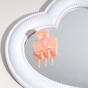 Macro detail of a pale peach acetate hair claw clip reflected on a heart-shaped mirror