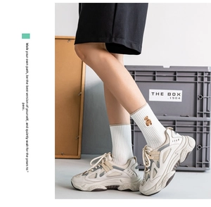 Detail of white cotton mid-calf socks featuring a cute bear embroidery with chunky sneakers
