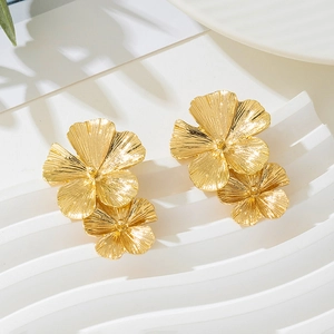 Close-up of golden textured double flower stud earrings on a white elegant display