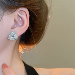 Macro shot of silver cross triangle stud earrings with shimmering cubic zirconia on ear