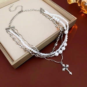 Close-up of multilayer silver necklace with pearls and cross pendant on beige jewelry box