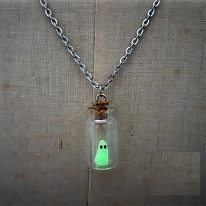 Glow-in-the-dark green ghost inside a glass drift bottle necklace on a beige display