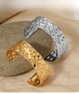Detail of irregular textured wide open bangles in gold and silver on natural stone