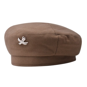 Detail shot of brown wool beret featuring a metallic cross-shaped side decoration