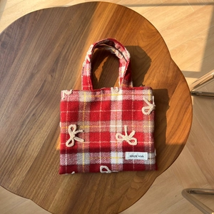Vue détaillée du sac à main en tweed à carreaux rouges avec nœuds au crochet sur bois rétro