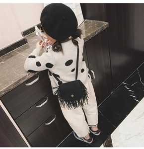 Detail of child wearing a black suede tassel crossbody bag with golden metal buckle
