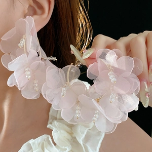 Gros plan de boucles d'oreilles créoles dorées avec fleurs en résille rose et perles de cristal