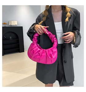 Macro shot of a vibrant pink pleated cloud bag on a textured black blazer background