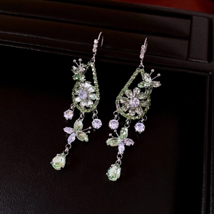Macro detail of silver-tone flower and butterfly earrings with green zircon teardrops