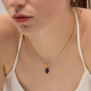 Golden titanium steel beaded necklace with a geometric dark blue crystal pendant on a model