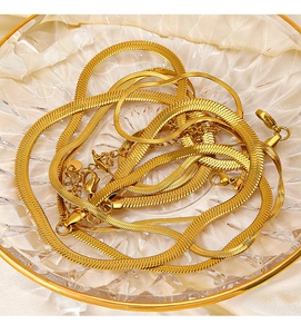 Detailed close-up of glossy 18K gold plated snake chain necklaces on silk fabric