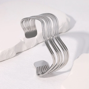 Minimalist silver wavy stainless steel bangle displayed on white geometric stone background
