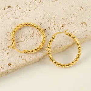 Retro golden twisted rope hoop earrings displayed on a textured stone decorative base