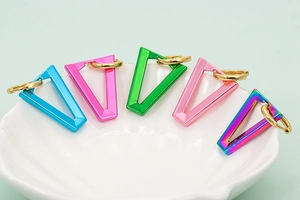 Macro shot of colorful V-shaped enamel triangle earrings in a white textured ceramic dish