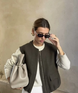 Detailed view of deep brown zip-up vest paired with a cream sweater and leather handbag