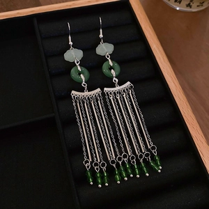 Detail of silver long tassel earrings with green jade-like beads on black velvet