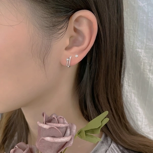 Close-up of minimalist silver paperclip earrings with a bead stud on model ear