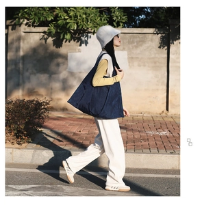Outdoor street style view of a large navy blue canvas shoulder bag worn by a model