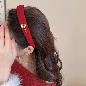 Gros plan d'un serre-tête en velours rouge foncé avec un ornement en métal camélia doré