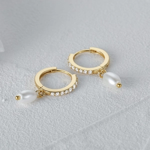 Macro detail of gold pearl earrings featuring white zircon and water-drop pearl charms