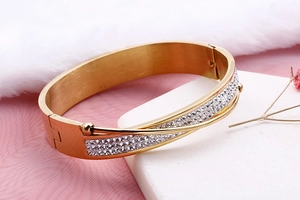 Close-up of golden wide brushed stainless steel bangle with pavé crystals and ball clasp