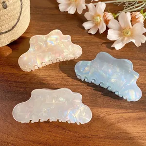 Three colorful cloud-shaped hair claws in pink, blue and beige on a wooden surface
