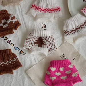 Detailed view of knitted doll sweaters with various colorful patterns on white fabric