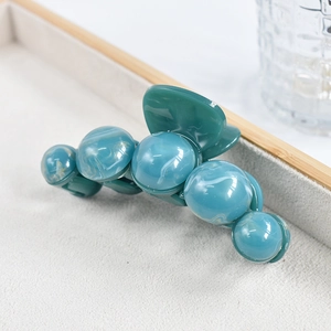 Detail of teal marble texture hair claw clip with faux pearls on a display tray