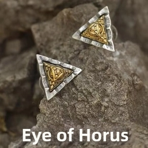 Macro shot of silver Eye of Horus triangular earrings on vintage textured rock