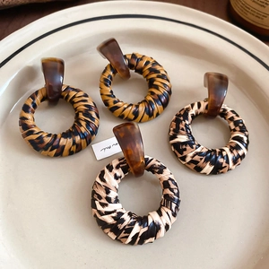Close-up of leopard print woven hoop earrings with resin studs on a porcelain tray